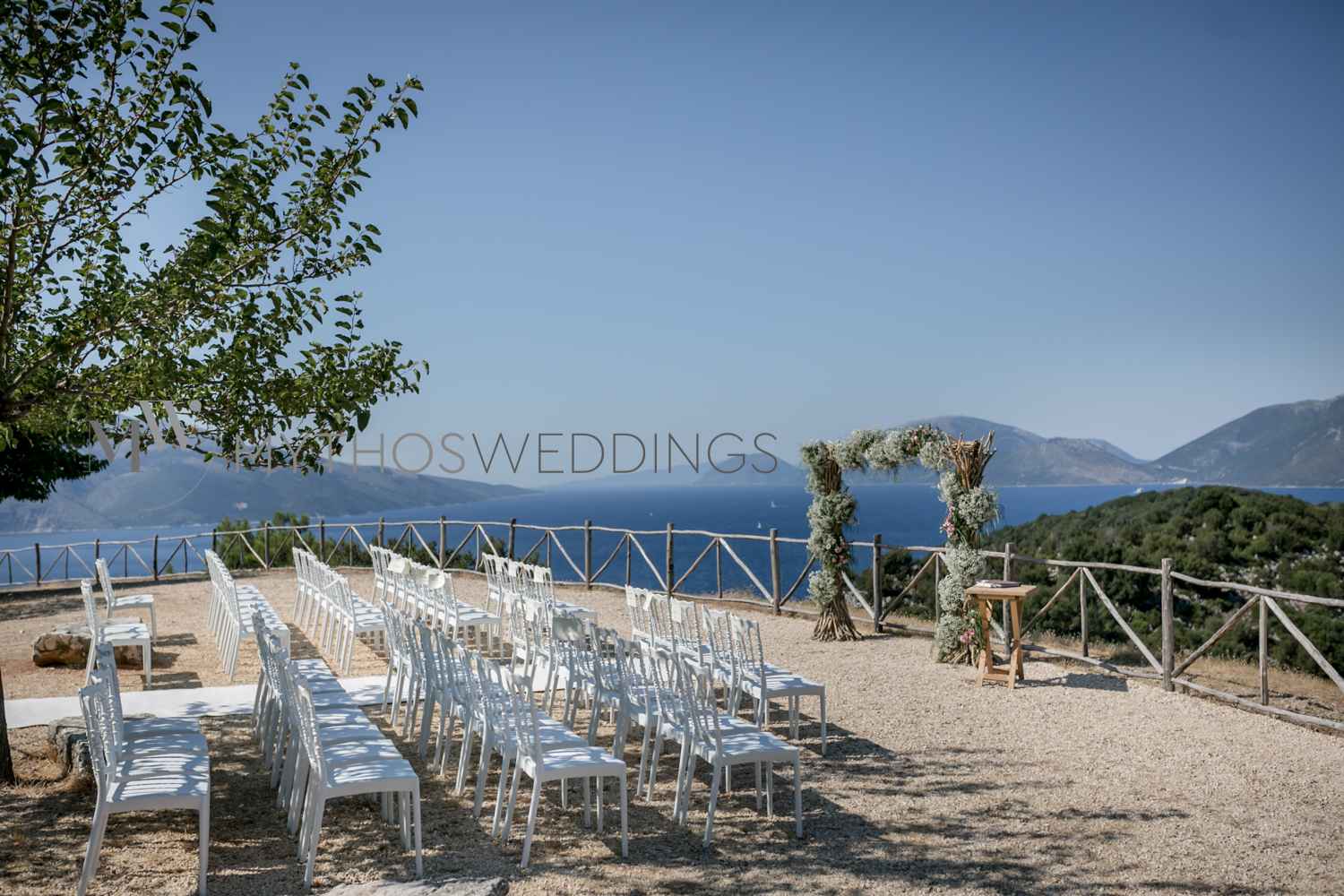 Weiße Stühle und ein Hochzeitsbogen unter blauem Himmel
