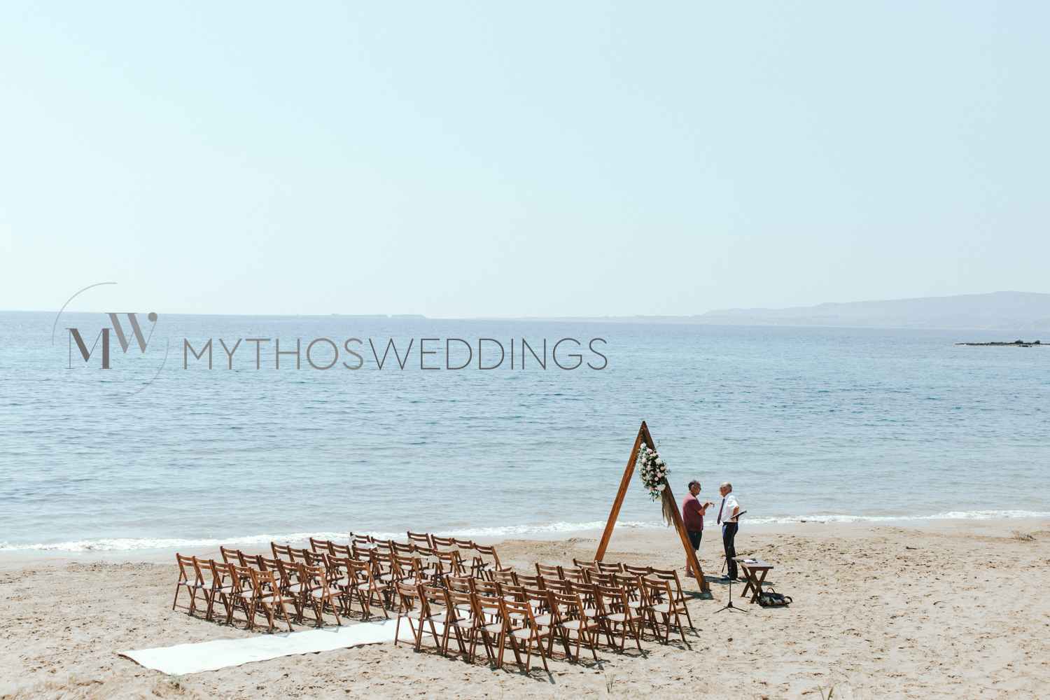 Holzstühle und ein Hochzeitsbogen am Strand