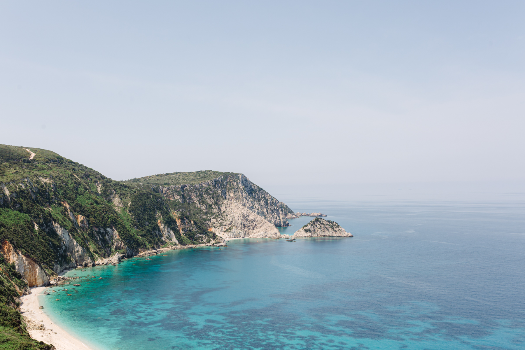 blick von oben auf eine Bucht mit weißem Sand und türkisem Meer, umrahmt von grün bewachsenen Felsen