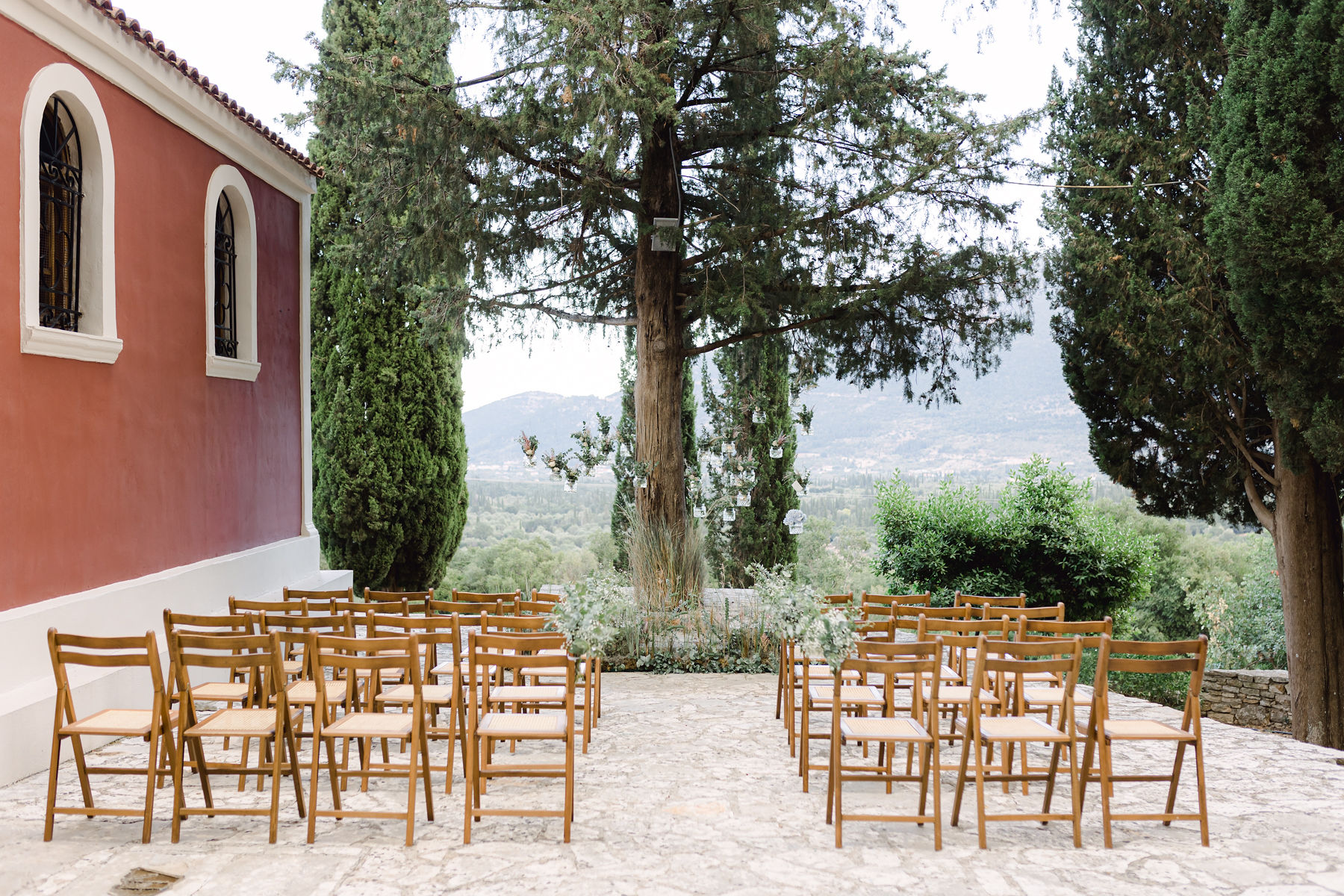 Aufbau einer freien Trauung mit braunen Stühle neben roter Kapelle und zwischen Pinienbäumen