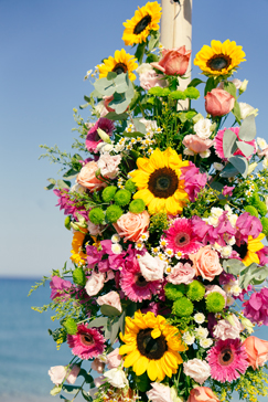 Blumenarrangement vom Traubogen mit Sonnenblumen und pinken Blüten mit Meer im Hintergrund