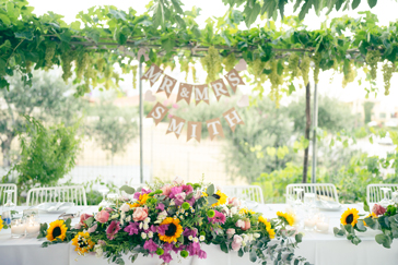 mit Blumenarrangement gedeckte Hochzeitstafel in Griechenland, darüber Hochzeitsgirlande