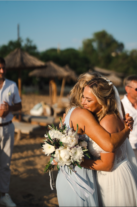 Braut wird von Brautmutter am Strand von Griechenland umarmt.