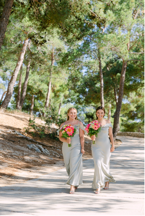 Brautjungfern gehen einen Weg entlang, hohe grüne Nadelbäume im Hintergrund