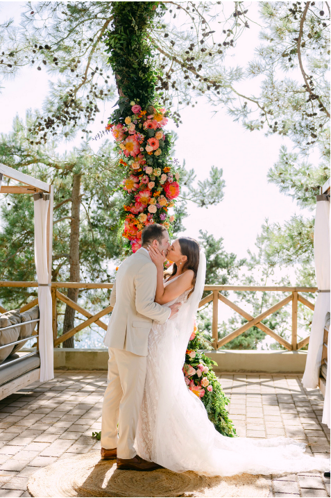 küssendes Brautpaar vor Blumengirlande in pink